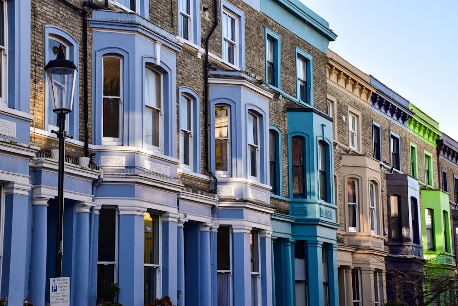 The image depicts a row of four to five-story Victorian-style residential buildings with ornate architectural features, including bay windows, decorative moldings, and small balconies, painted in past